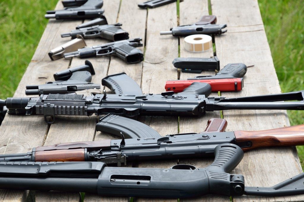 A shotgun, pistols and other firearm are laid out on the table outdoors