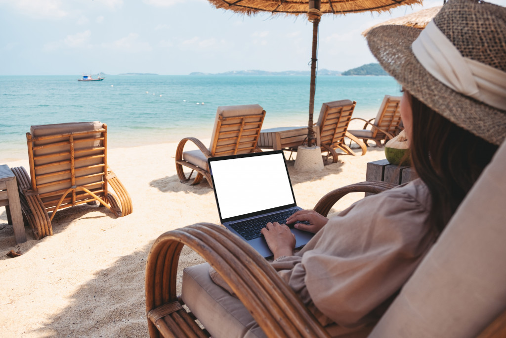 a young woman sitting on the beach while typing on her laptop