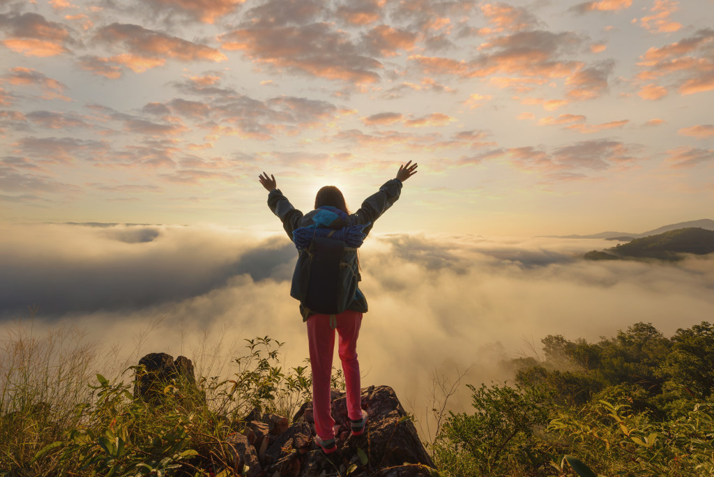 a woman on top of a hill with hands in the sky