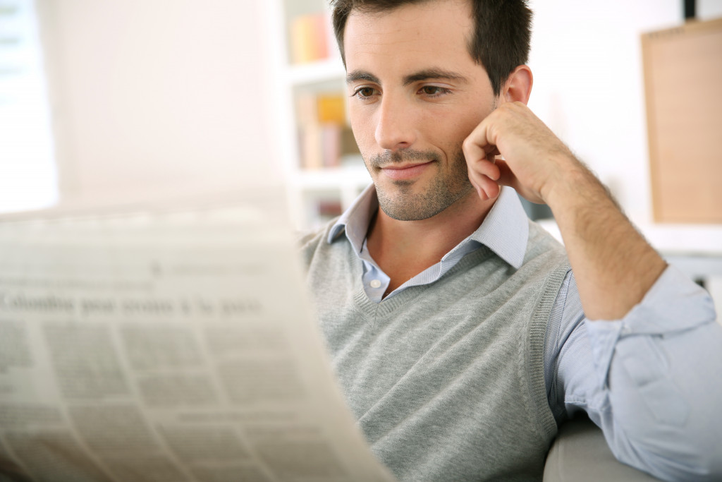 A Young Man Holding a Newspaper in a Sofa at Home