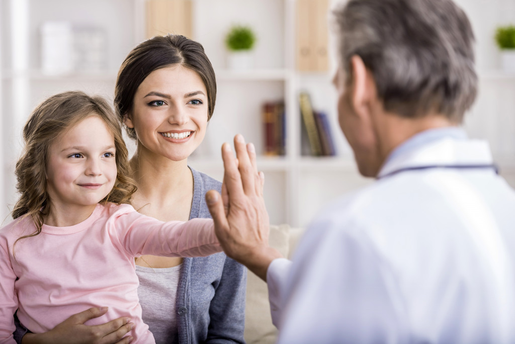 a little girl with her mother doing a high five with a doctor