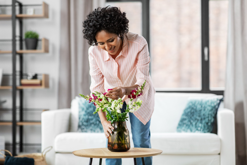 a woman placing plants and flowers at a vase at home