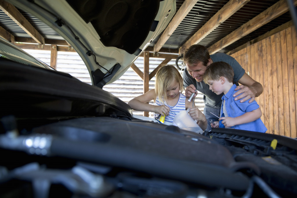 A father letting his children help him with his car in the garage