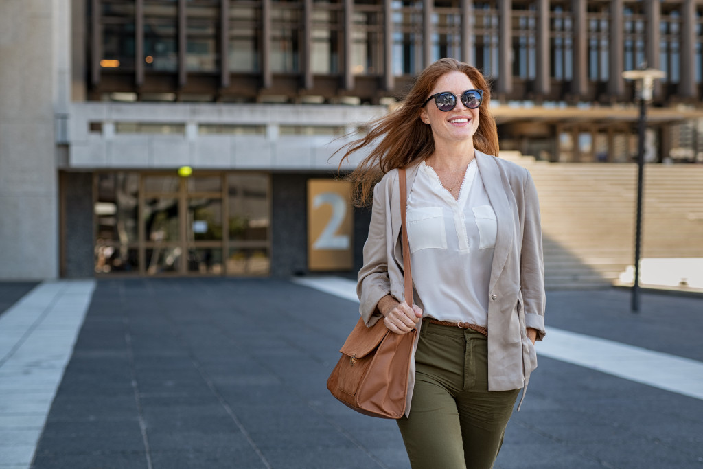 a confident woman walking outdoors with a brown bag and sunglasses