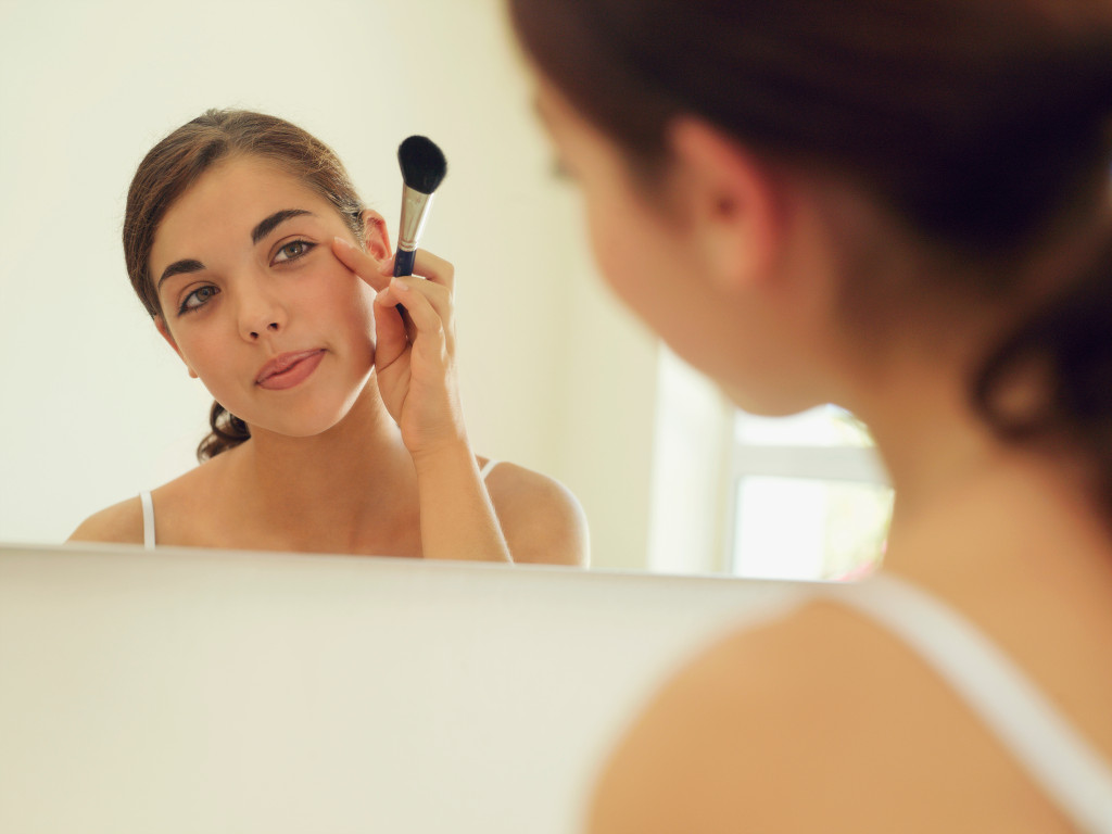 A woman looking at herself in the mirror, applying makeup