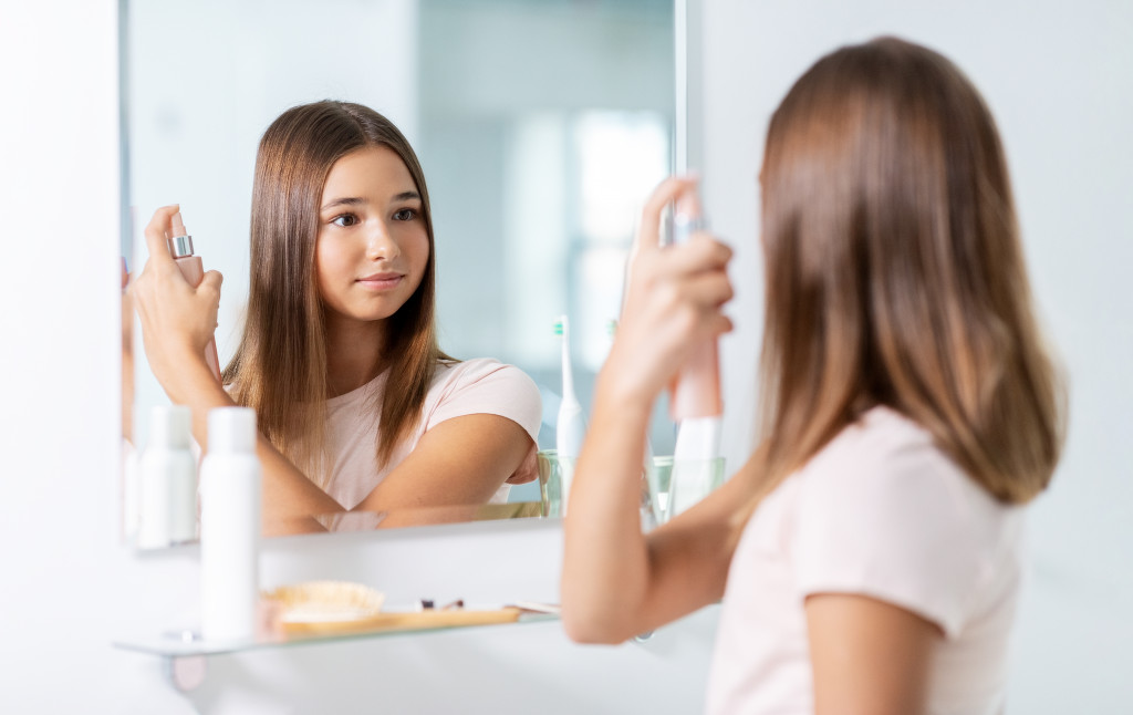 A woman looking in the mirror while applying styling spray on her hair