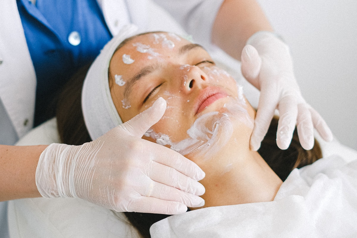 Cosmetologist applying facial mask on customer face in spa salon