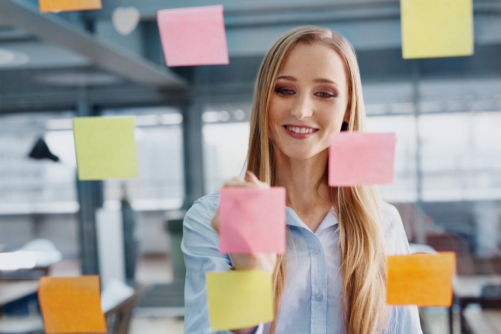 A woman writing on sticky notes on a glass wall