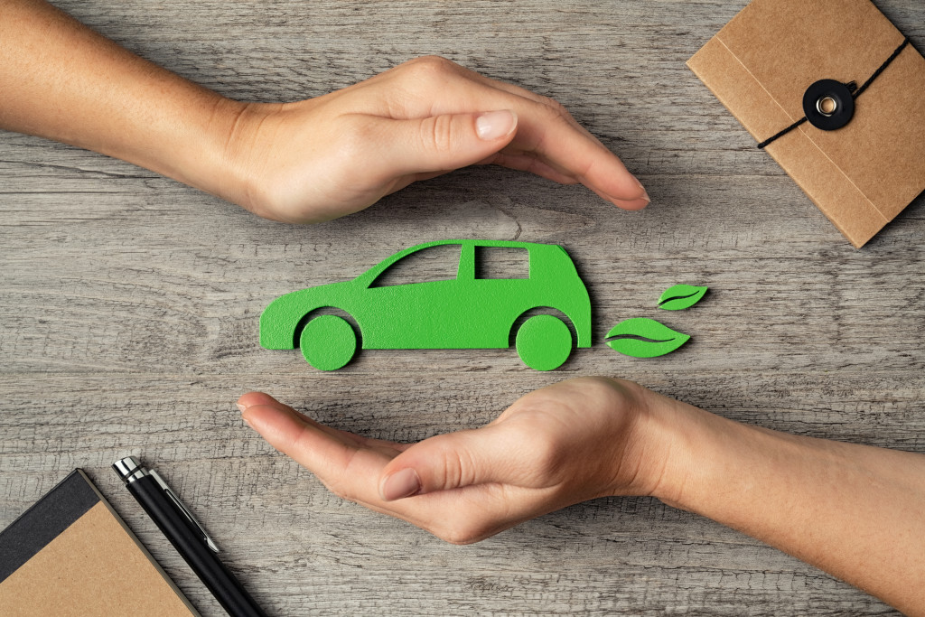 two hands holding green car model with leaves at the tail