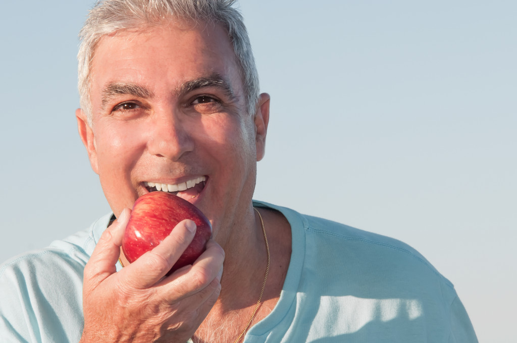 Male senior happily eating an apple outdoors.