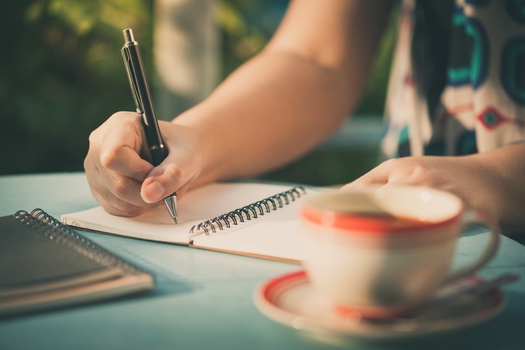 A woman writing on a notebook in a coffee shop