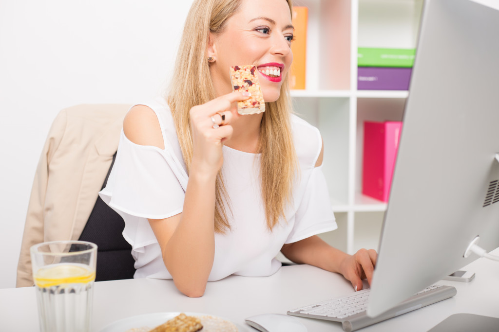 A woman eating a granola bar while working