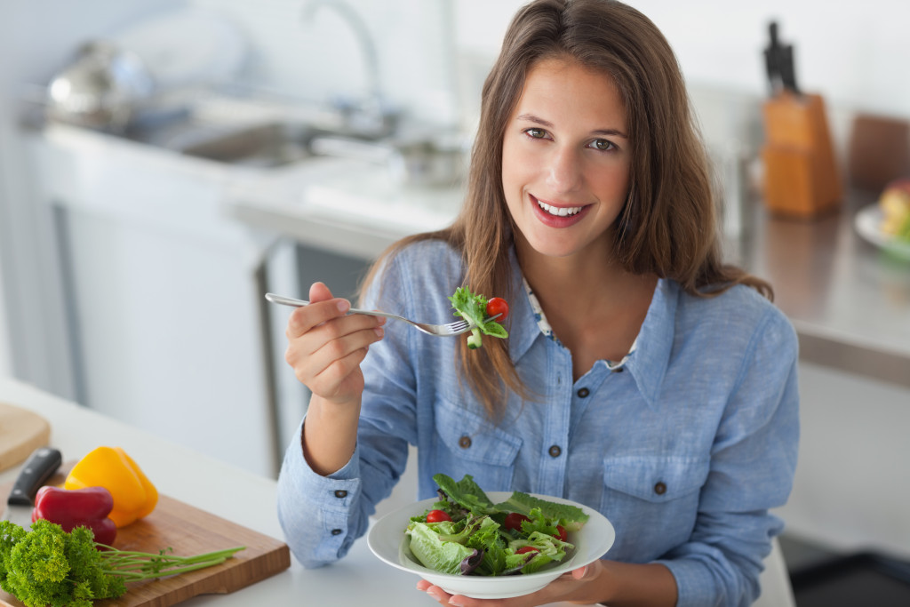 woman smiling while holding fork with green salad in bowl