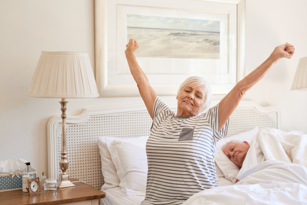 A senior woman stretching her arms while sitting on a bed