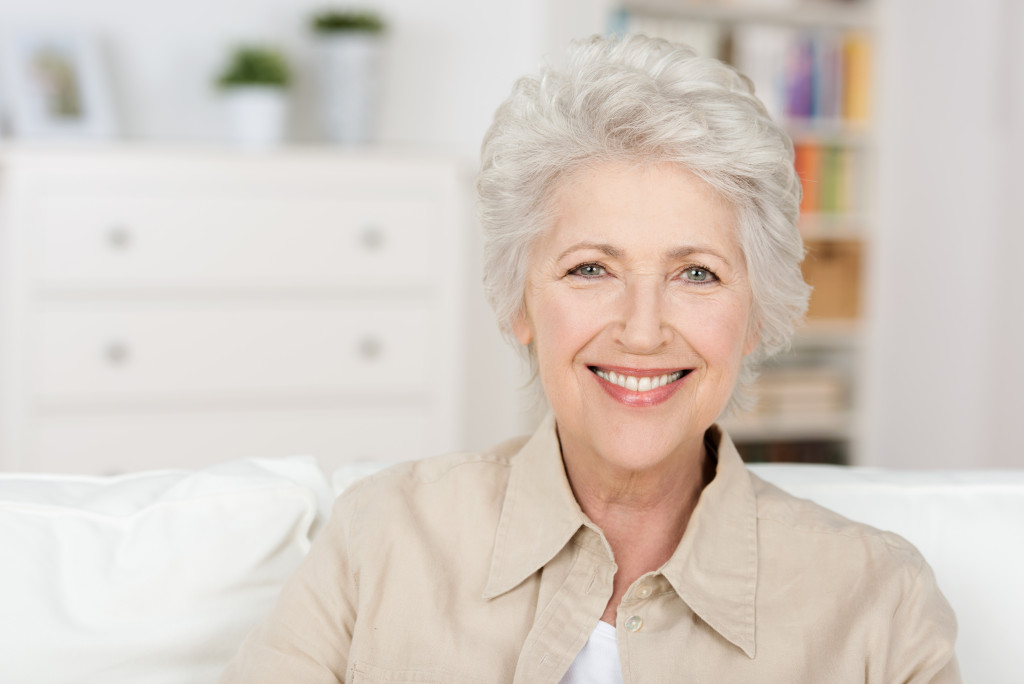 smiling senior woman in her minimalist majorly white living room couch