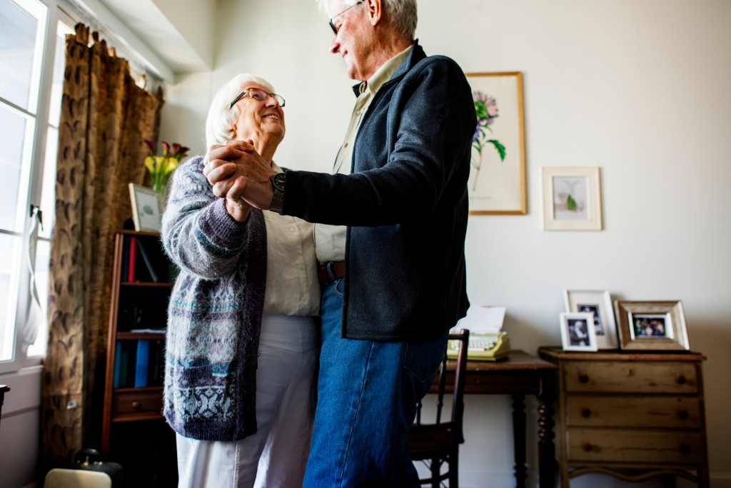 elderly couple smiling while dancing in their living room